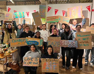 Participants in a community research field trip hold up hand-painted placards sharing messages about the issues that matter to them.